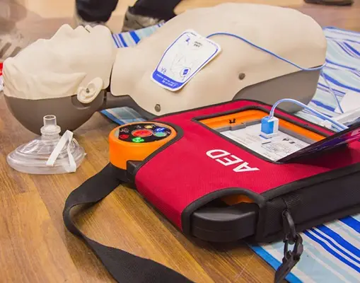 CPR Training Equipment With Manikin And AED on Wooden Floor